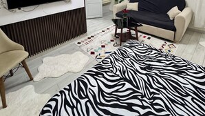 Ett modernt vardagsrum med en platt-TV som är monterad på en vägg av marmor, en soffa, en mönstrad matta och en dekorativ lampa.