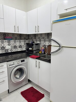 A compact kitchen with white cabinets, a washing machine, a refrigerator, and patterned backsplash tiles. - Cosy F2 apartment in the heart of Algiers (Alger Centre)