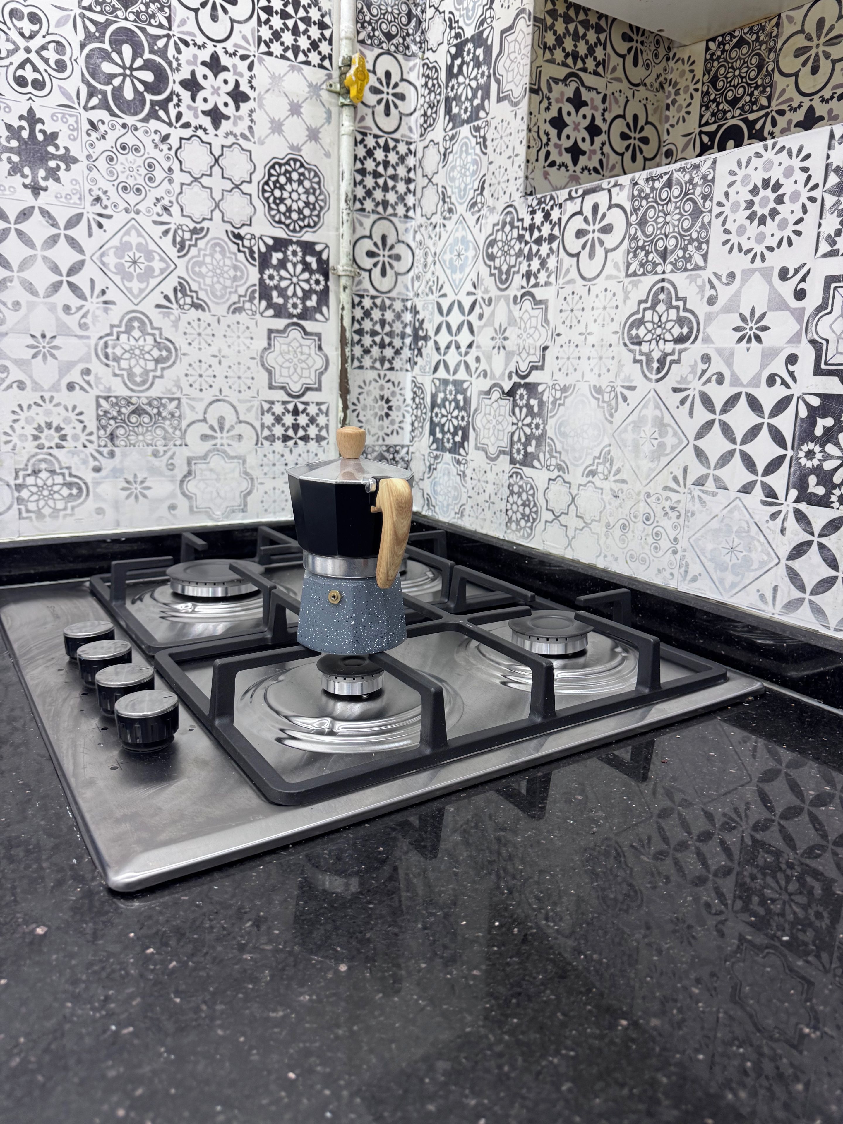 A kitchen with a gas stove, a coffee maker, and a patterned backsplash.