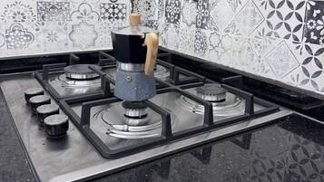 A kitchen with a gas stove, a coffee maker, and a patterned backsplash.