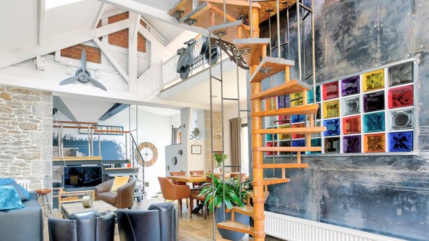 Un vaste espace de vie doté d’un haut plafond, d’un escalier en bois et d’un mur décoré de carreaux colorés.