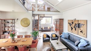 Un vaste espace de vie doté d’un haut plafond, d’une table à manger en bois, de canapés en cuir et d’un escalier menant à un niveau supérieur.