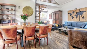 Un vaste espace de vie comprenant une table à manger en bois, des fauteuils en cuir, un canapé et une décoration murale représentant une carte du monde.