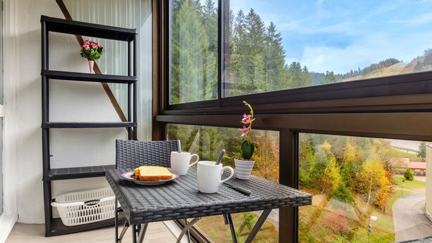 A balcony with a wicker table, two white mugs, a plate with a slice of cake, and a potted plant. - Kamélia - 10min des pistes (La Bresse)