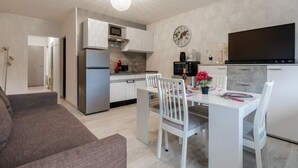 A modern kitchen with a dining area, including a white table, chairs, and a sofa. - Kamélia - 10min des pistes (La Bresse)