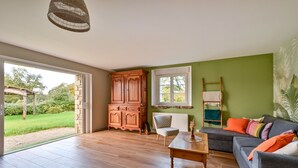 Ein geräumiges Wohnzimmer mit Holzboden, einem grauen Sofa mit bunten Kissen, einem Holzschrank und einem Sessel.