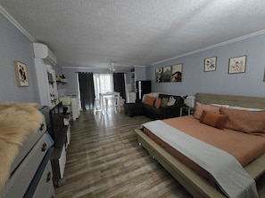 A bedroom with a bed, a desk, a chair, a sofa, and a kitchenette.