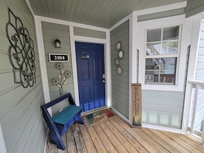A wooden porch with a blue door, a bench, and a welcome sign.