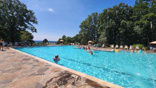 A swimming pool with clear blue water, surrounded by trees and a stone deck. - Lake Escape Getaway (Fairfield Bay)
