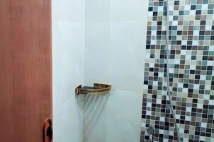 Un baño con paredes de azulejos blancos, una puerta de madera y una zona de ducha con un mosaico de azulejos.