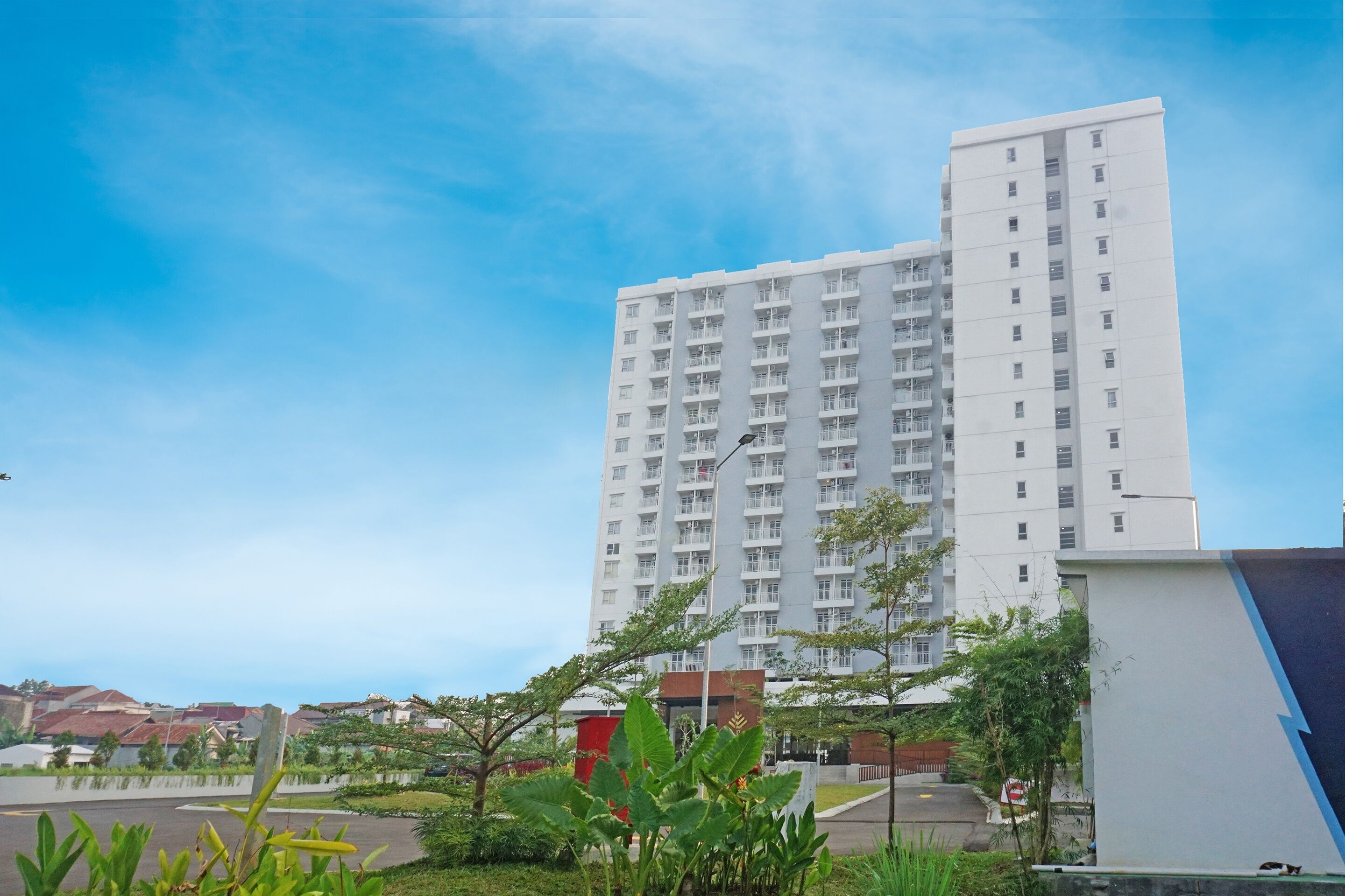 A tall white building with multiple floors, surrounded by greenery and a clear sky.