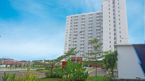 A tall white building with multiple floors, surrounded by greenery and a clear sky.