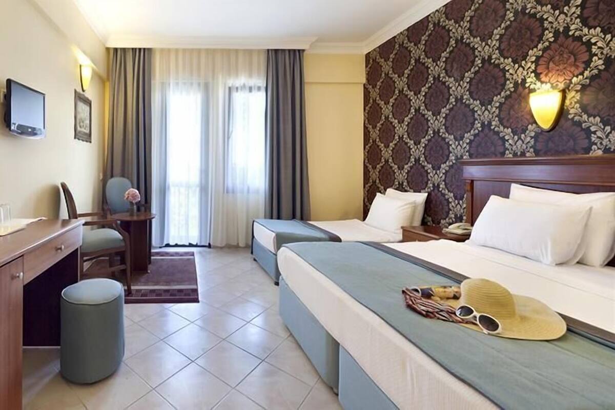 A hotel room with a bed, a desk, a chair, a small stool, a television, and a patterned wall.
