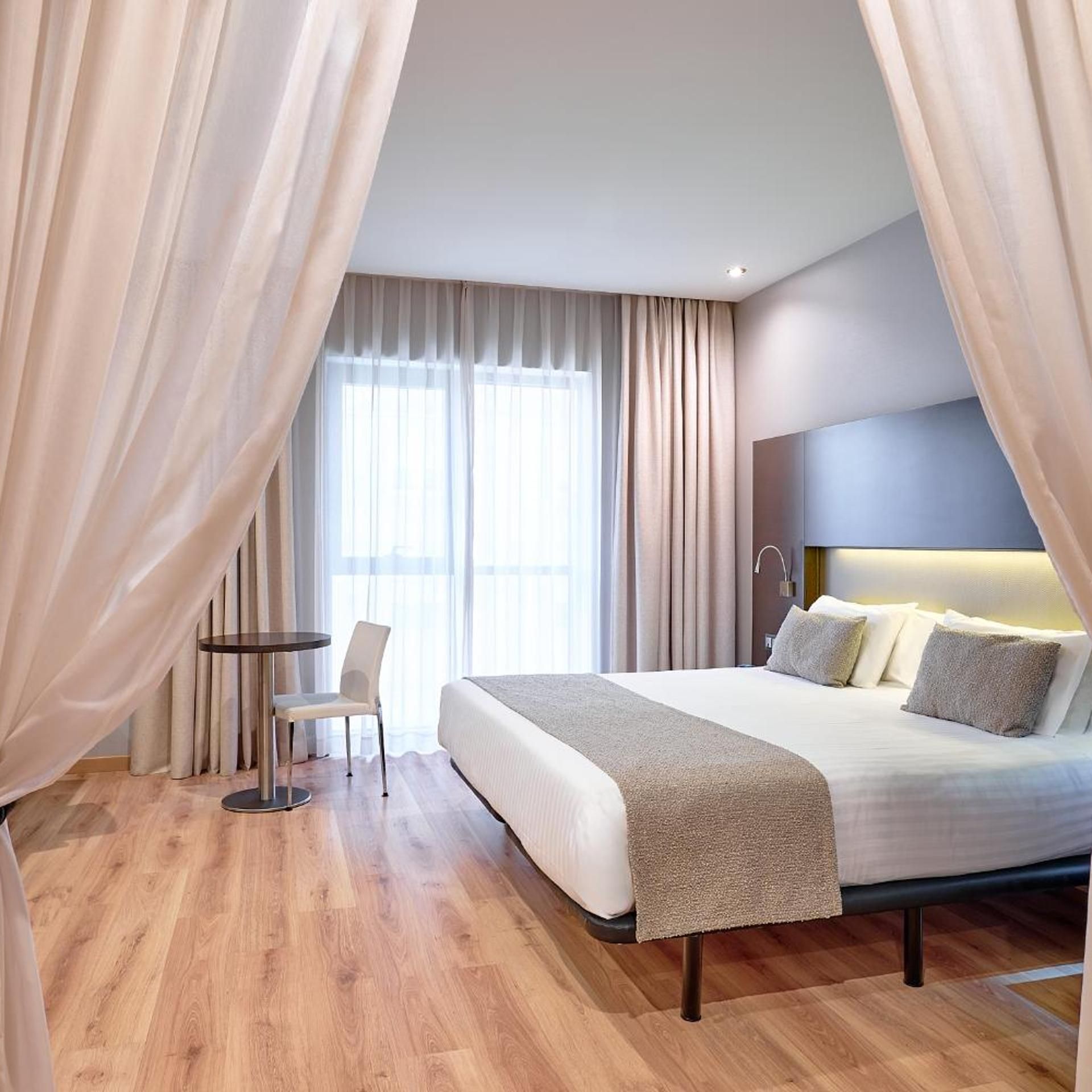 A hotel room with a bed, bedside table, chair, and curtains.
