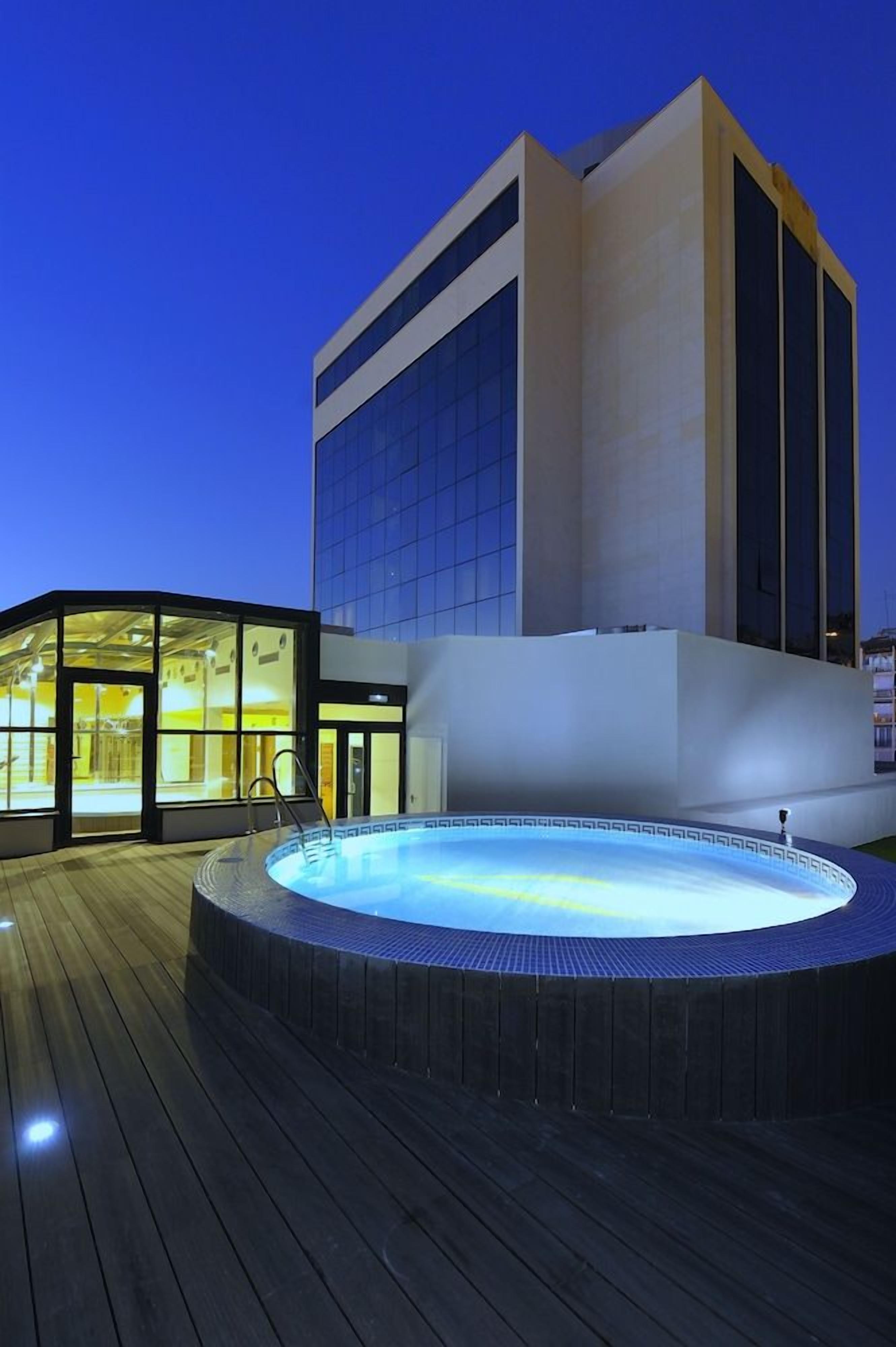 A modern building with a glass facade and a hot tub area with a wooden deck.