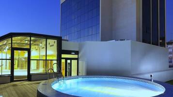 A modern building with a glass facade and a hot tub area with a wooden deck.