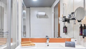 Un baño moderno con cabina de ducha de vidrio, un lavamanos blanco con espejo y artículos de aseo en la pared.