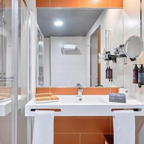 Uma casa de banho moderna com cabine de duche em vidro, uma sanita branca com espelho e artigos de higiene pessoal na parede.