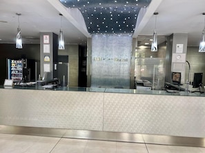 A reception area with a glass counter, a vending machine, and a wall-mounted sign. - Hotel Turia Granada (Granada)