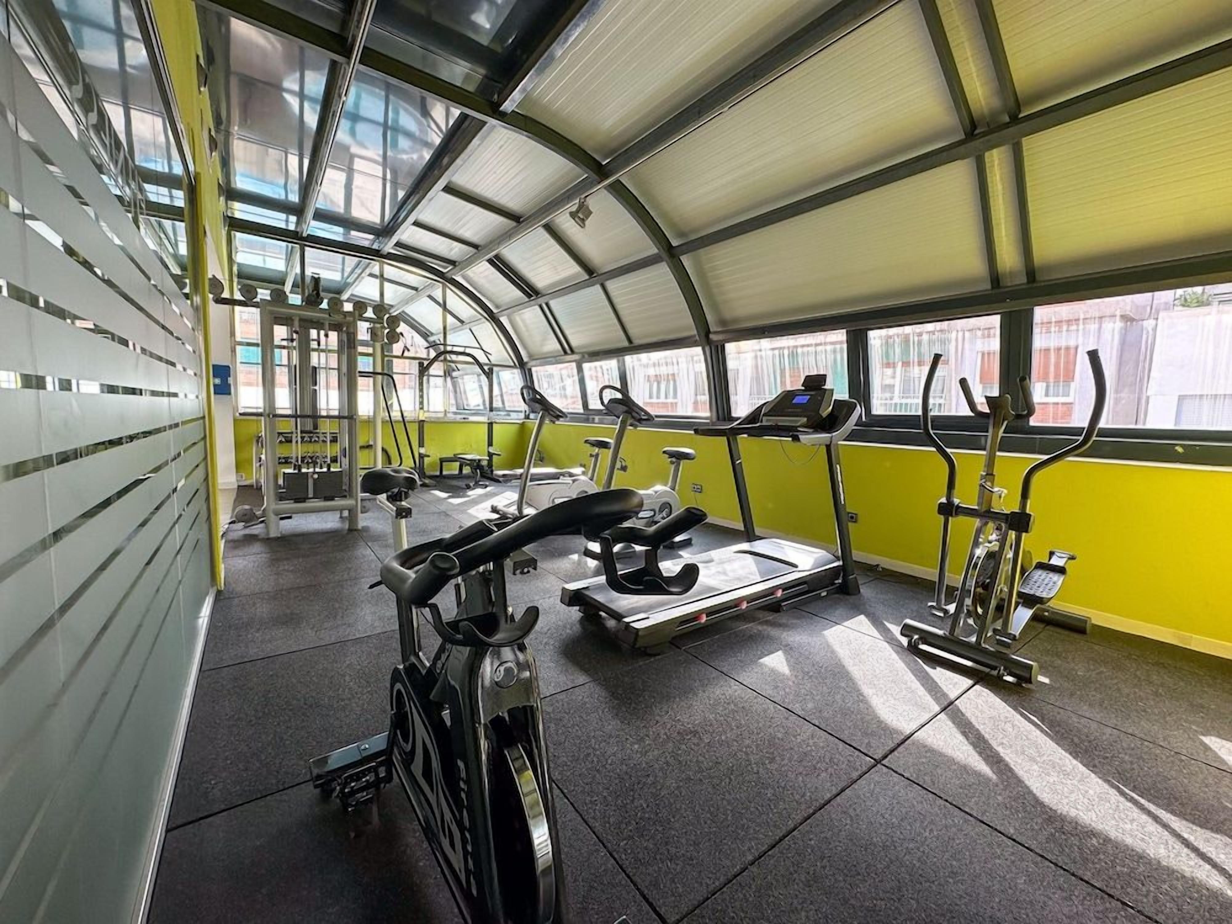 Ein Fitnessstudio mit Trainingsgeräten, darunter Laufbänder und ein Ergometer, unter einer Glasdachkonstruktion.