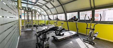 Een fitnessruimte met trainingsapparatuur, waaronder loopbanden en een hometrainer, onder een glazen dak.