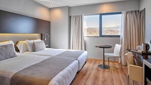 Habitación de hotel con dos camas, una mesita pequeña, una silla, un escritorio y una ventana con cortinas.