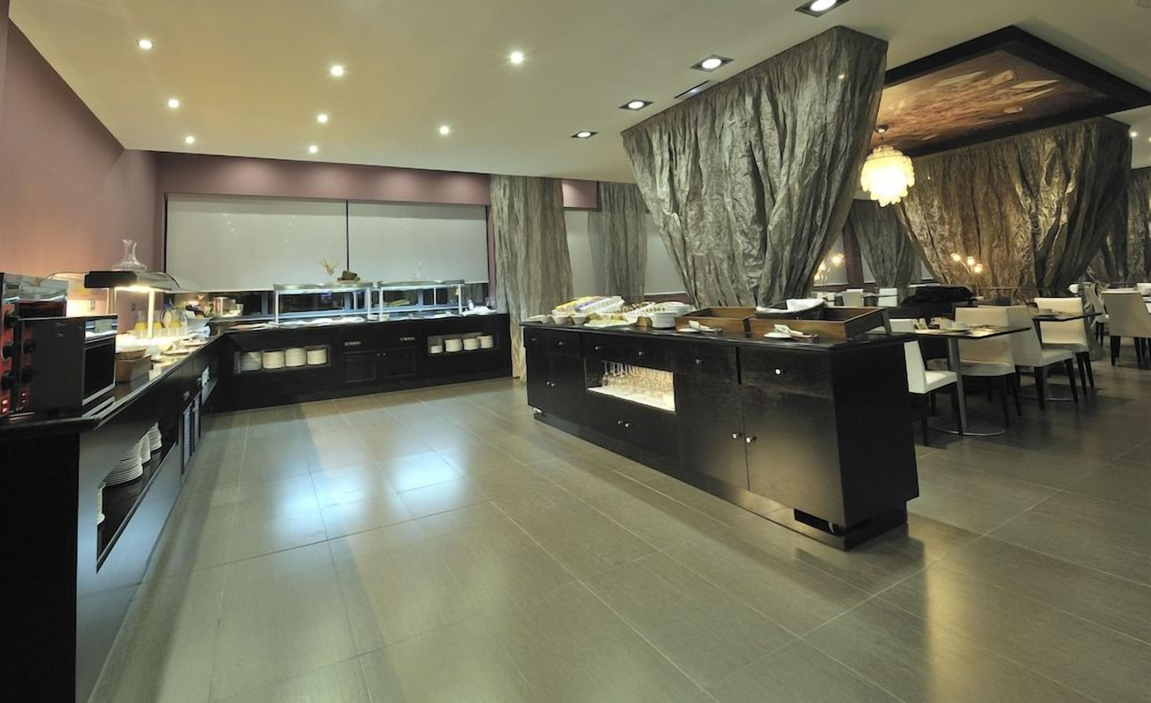 Un comedor moderno con una estación de buffet central, arreglos de asientos y un amplio ventanal.