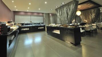 Un comedor moderno con una estación de buffet central, arreglos de asientos y un amplio ventanal.