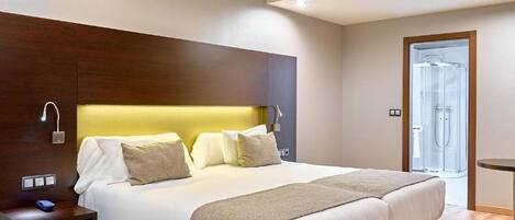 Une chambre d’hôtel moderne avec un grand lit, des tables de chevet, une tête de lit en bois et une porte de douche en verre.