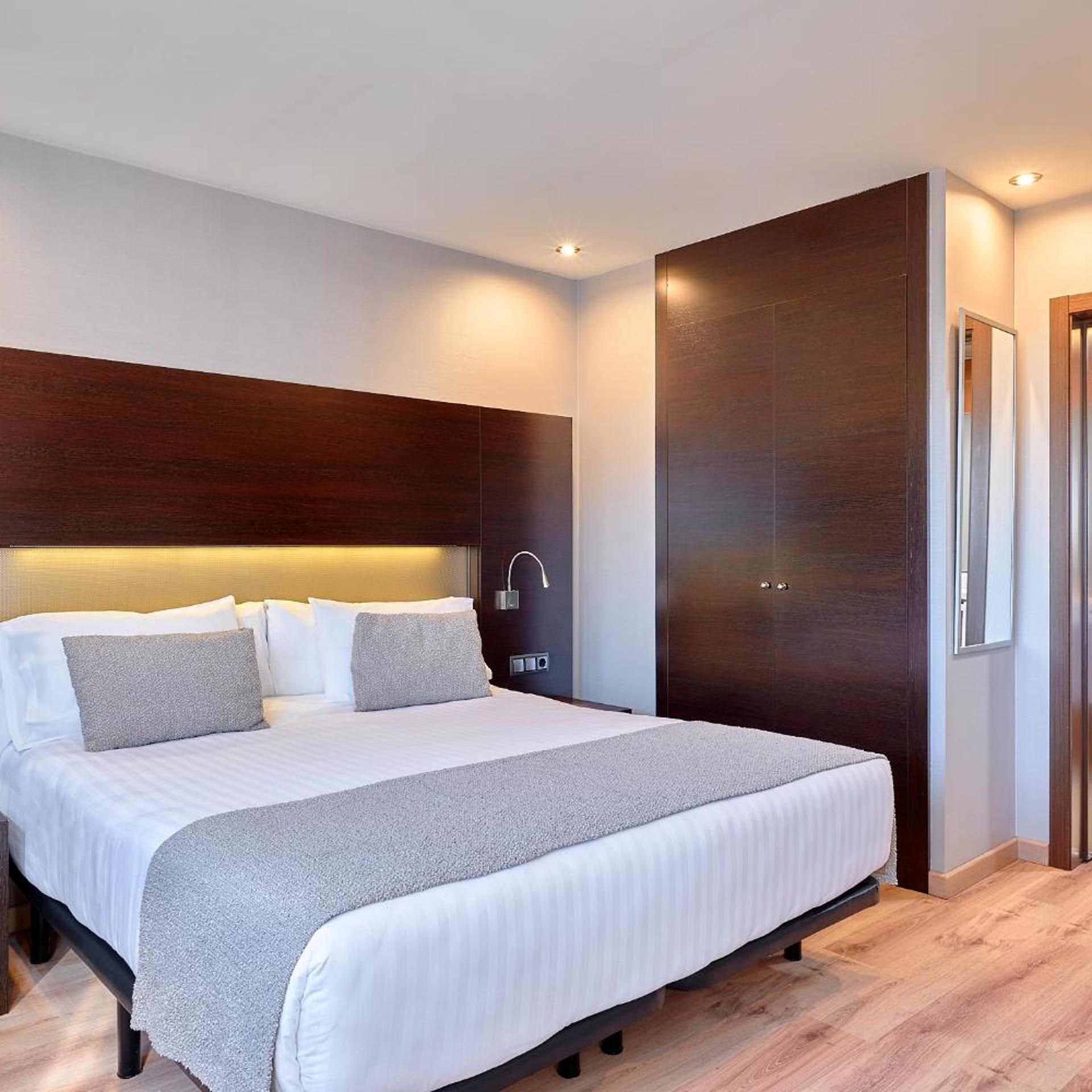 A modern hotel room with a large bed, a wooden headboard, a bedside table, and a wardrobe.