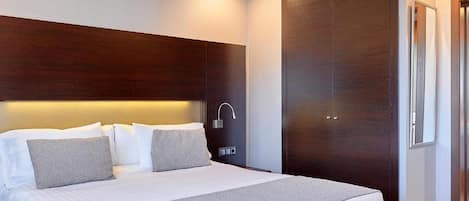 A modern hotel room with a large bed, a wooden headboard, a bedside table, and a wardrobe.