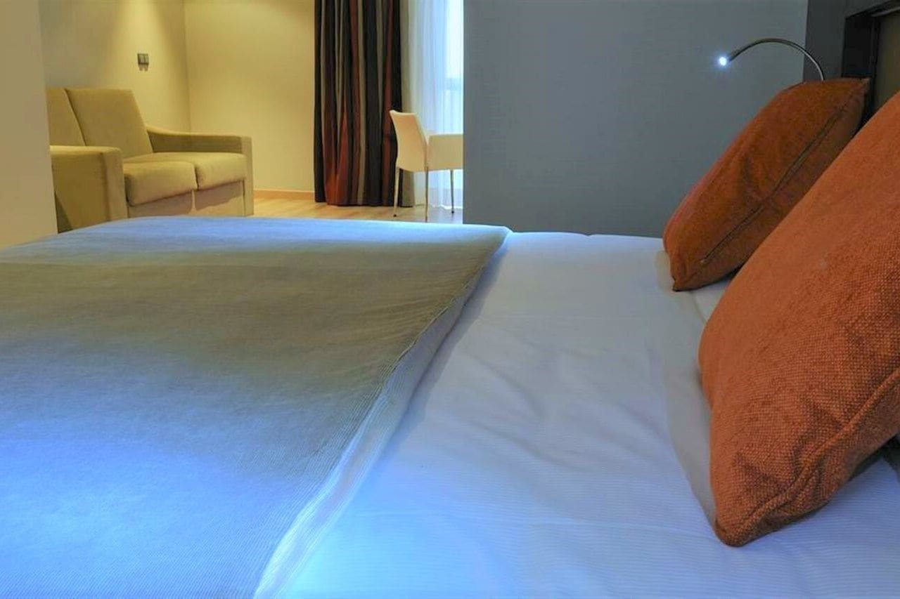 A hotel room with a bed, a chair, and a lamp.