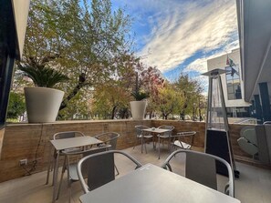 An outdoor seating area with tables and chairs, large potted plants, and a view of trees and a building in the background. - Hotel Turia Granada (Granada)