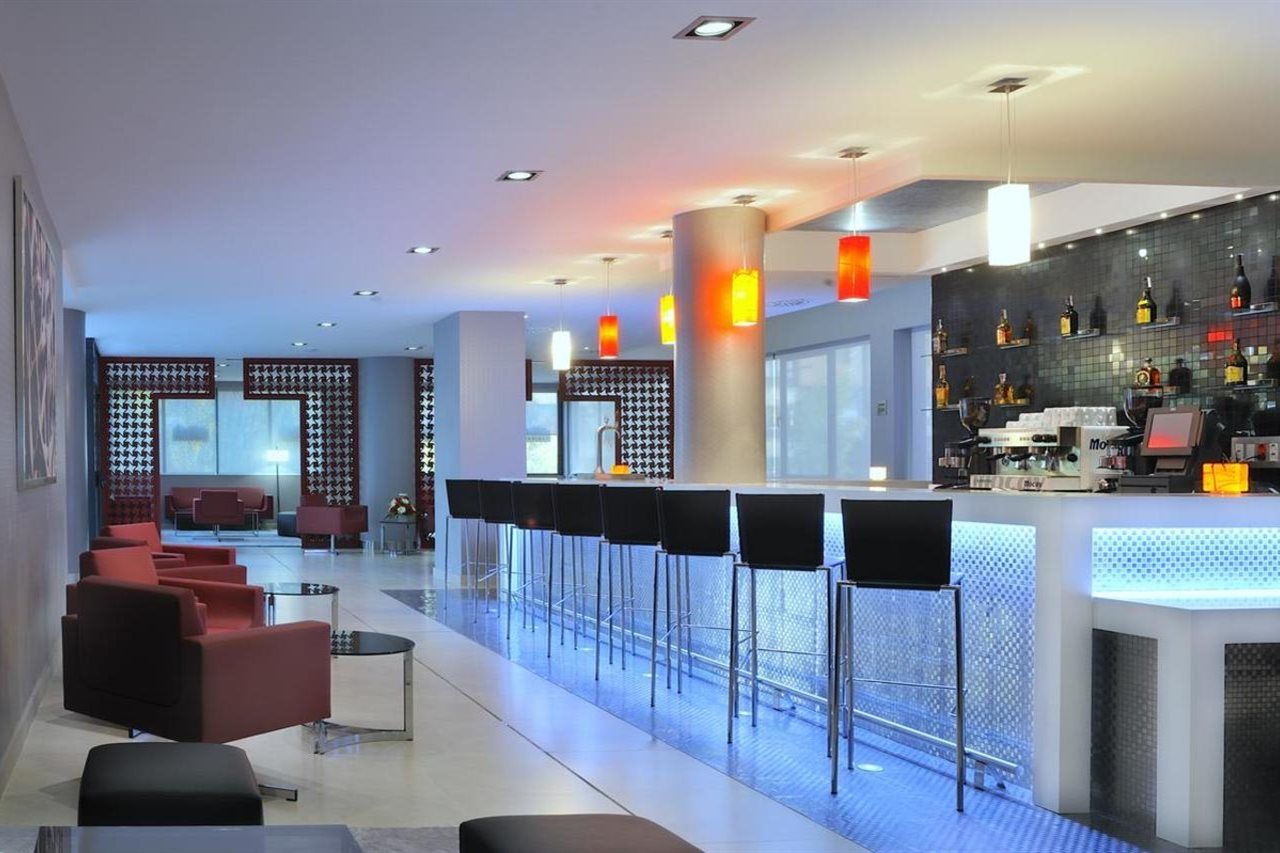 A modern bar area with a long counter, multiple bar stools, and a wall of liquor bottles.