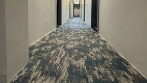 A long, narrow hotel corridor with a patterned carpet, white walls, and a ceiling light fixture. - Hotel Aryan Inn (Haridwar)