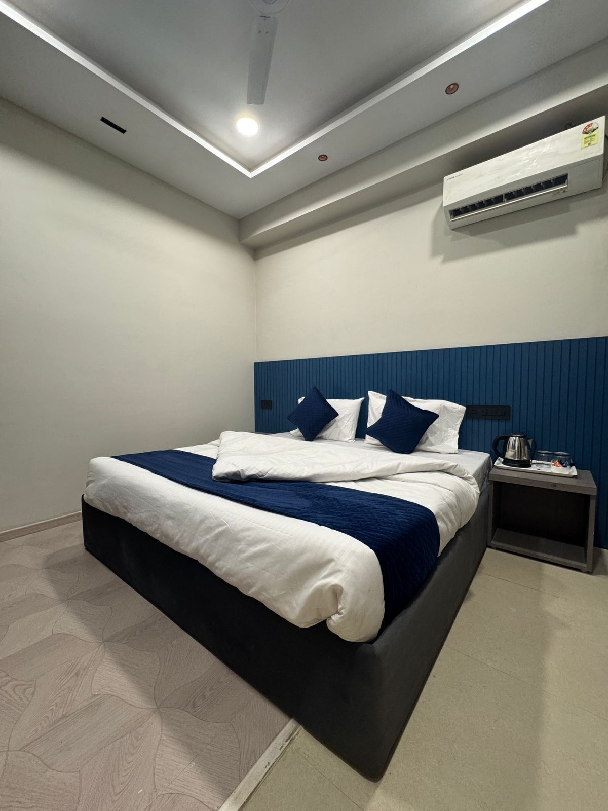 A modern hotel room with a large bed, a nightstand, an air conditioning unit, and a ceiling light.