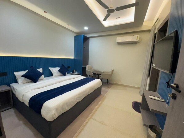 A modern hotel room with a large bed, a desk, a chair, and a TV. - Hotel Aryan Inn (Haridwar)