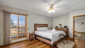 Un dormitorio con cama de madera, ventilador de techo, ventana grande y espejo.