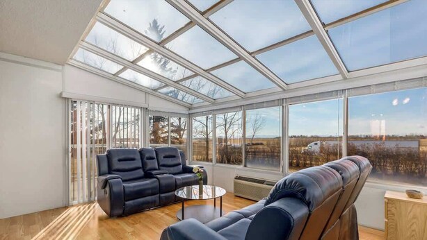 Una sala de estar moderna con techo de vidrio, sofás de cuero y vista a un paisaje nevado.