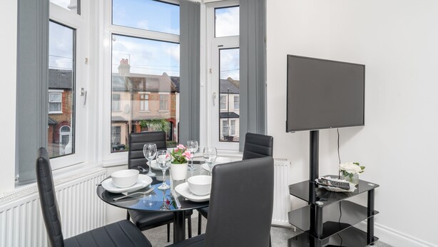 Un comedor con una mesa dispuesta para cuatro, un televisor de pantalla plana y vistas a la calle a través de amplias ventanas.