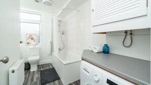Un baño moderno con inodoro blanco, bañera, ducha y lavadora Bosch.