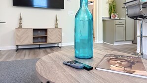 A living room with a TV, a large blue bottle, a remote control, and a magazine on a coffee table. - Modern 3BR Getaway Near Downtown Jacksonville (Jacksonville)