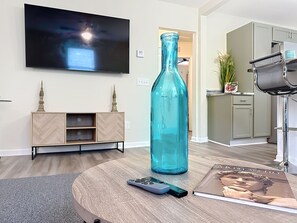 A living room with a TV, a large blue bottle, a remote control, and a magazine on a coffee table. - Modern 3BR Getaway Near Downtown Jacksonville (Jacksonville)