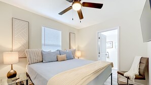 A bedroom with a bed, bedside lamps, a ceiling fan, a chair, and a door leading to another room. - Modern 3BR Getaway Near Downtown Jacksonville (Jacksonville)
