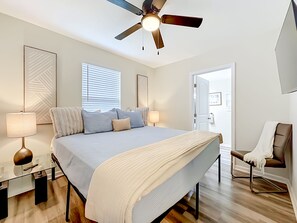 A bedroom with a bed, bedside lamps, a ceiling fan, a chair, and a door leading to another room. - Modern 3BR Getaway Near Downtown Jacksonville (Jacksonville)