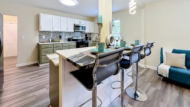 A modern kitchen with white cabinets, a stainless steel stove, and a dining area with a bar stool set. - Modern 3BR Getaway Near Downtown Jacksonville (Jacksonville)
