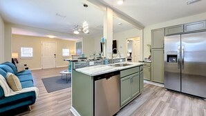 A modern kitchen with a central island, stainless steel appliances, and a dining area with a blue sofa. - Modern 3BR Getaway Near Downtown Jacksonville (Jacksonville)