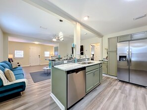 A modern kitchen with a central island, stainless steel appliances, and a dining area with a blue sofa. - Modern 3BR Getaway Near Downtown Jacksonville (Jacksonville)