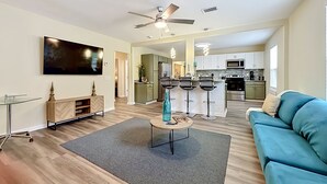 A modern living room with a sofa, a coffee table, a TV, and a kitchen in the background. - Modern 3BR Getaway Near Downtown Jacksonville (Jacksonville)