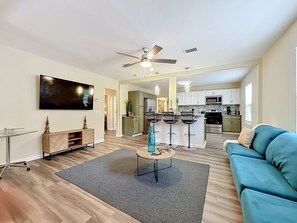 A modern living room with a sofa, a coffee table, a TV, and a kitchen in the background. - Modern 3BR Getaway Near Downtown Jacksonville (Jacksonville)